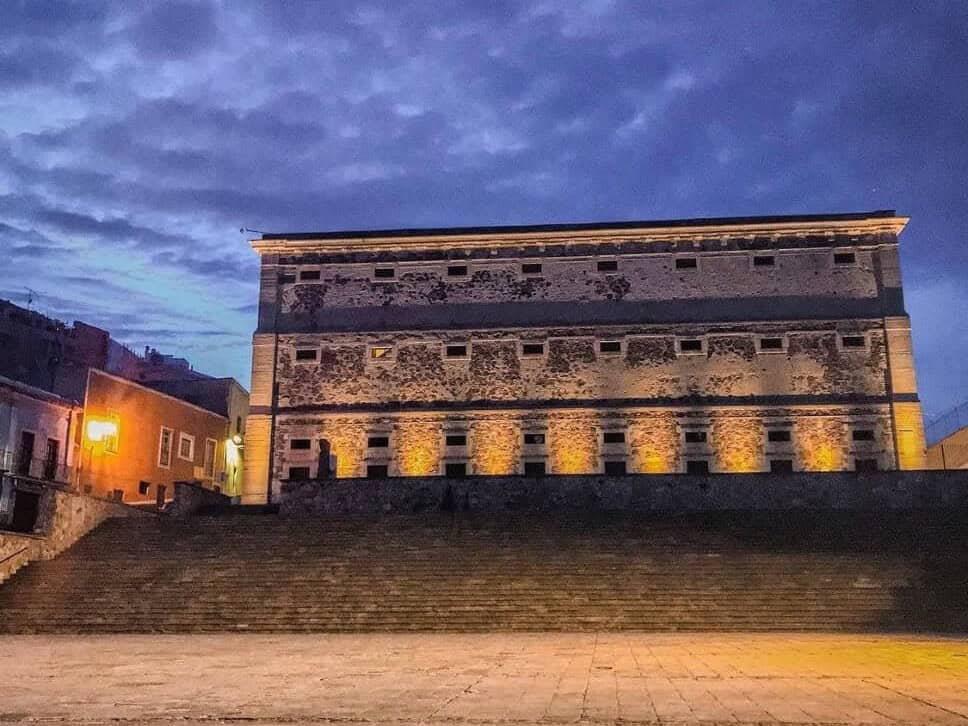 3. La Alhóndiga de Granaditas: historia y cultura en un solo lugar   Pocos edificios condensan tanta historia como la Alhóndiga de Granaditas, en la capital del estado. Construida a finales del siglo XVIII como granero público, el inmueble fue escenario de uno de los episodios más recordados del inicio de la independencia de México, cuando las fuerzas insurgentes tomaron el recinto en 1810. Hoy, el edificio funciona como museo regional y resguarda piezas arqueológicas, históricas y artísticas que narran la evolución de Guanajuato desde la época prehispánica hasta el siglo XX. Sus murales, obra del pintor José Chávez Morado, son una de las principales atracciones para quienes visitan el lugar, junto con la arquitectura del patio central y sus corredores. La Alhóndiga forma parte de la ruta obligada para quien recorre el centro histórico de la ciudad, declarado Patrimonio de la Humanidad por la UNESCO, y es frecuentemente incluida en recorridos guiados y visitas escolares que buscan acercar a las nuevas generaciones a la historia del estado. Su ubicación, a unos pasos del Jardín de la Unión, facilita combinar la visita con otros puntos emblemáticos de la capital